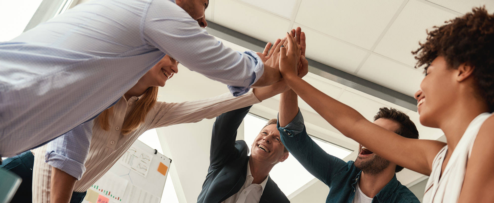 Fünf Personen geben sich in einem modernen Büro ein High-Five und lächeln.